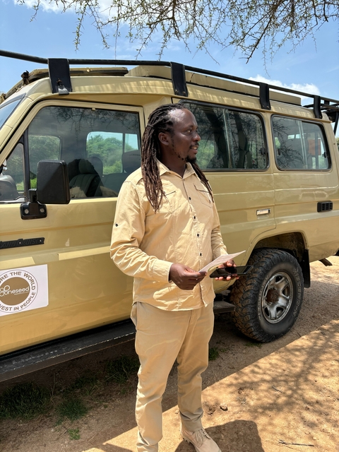 Tour guide standing beside a safari vehicle holding a brochure.