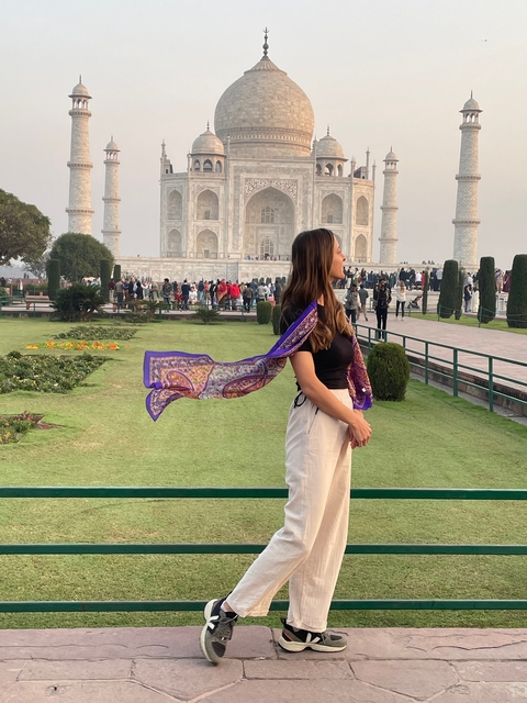 A woman standing in front of the Taj Mahal with a crowd in the background.