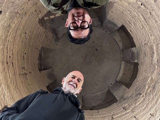       Two people looking down inside a round stone structure.
  
