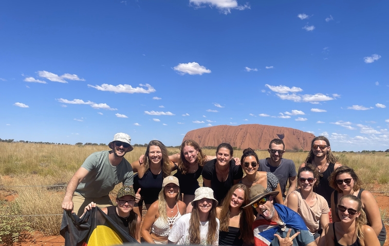 Group of people posing with Uluru in the background.