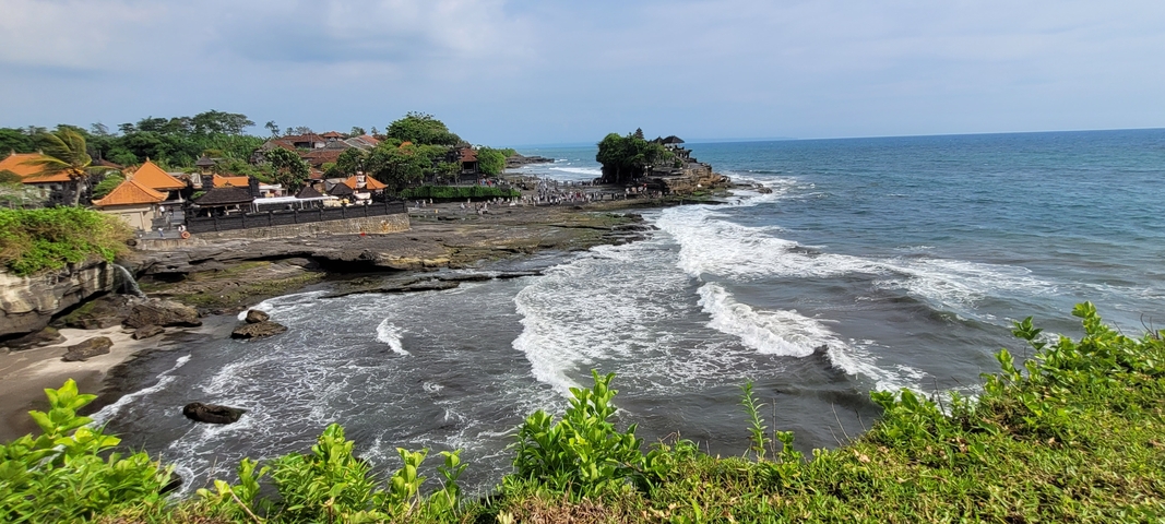 A view of a temple complex by the sea with waves hitting the shore.