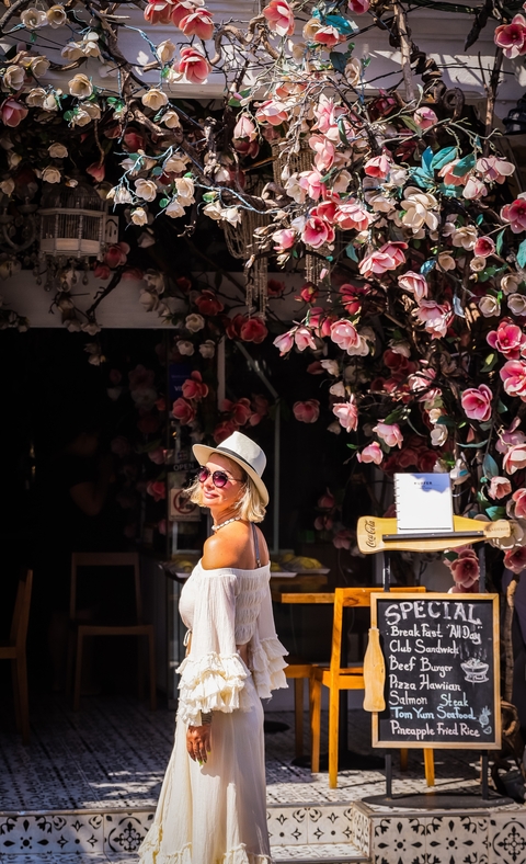       Woman in a hat posing in front of a floral display.
  