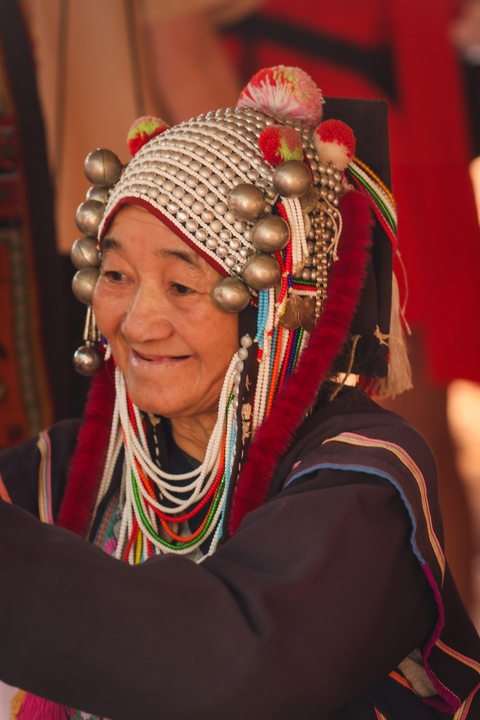       Elderly woman in traditional attire with beads and headdress
  