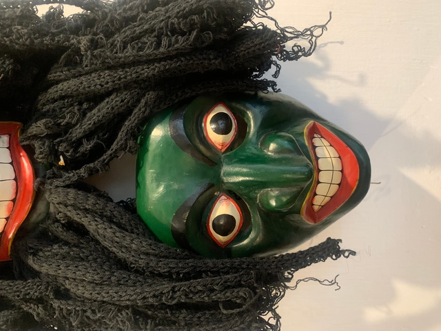       Colorful wooden masks with elaborate hairpieces displayed on a wall.
  