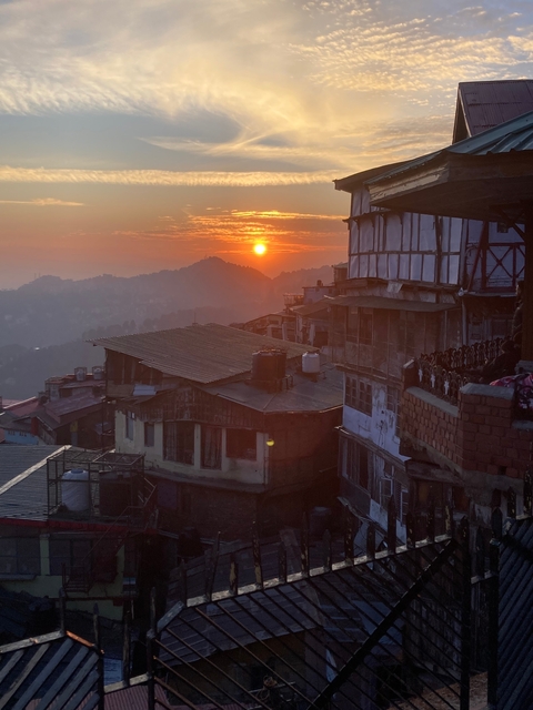Sunset view over a hilly cityscape with orange sky and silhouetted buildings.