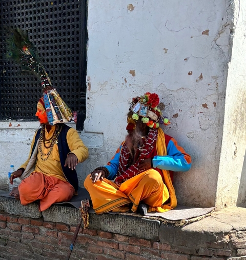 Two individuals dressed in colorful traditional attire sitting against a wall.