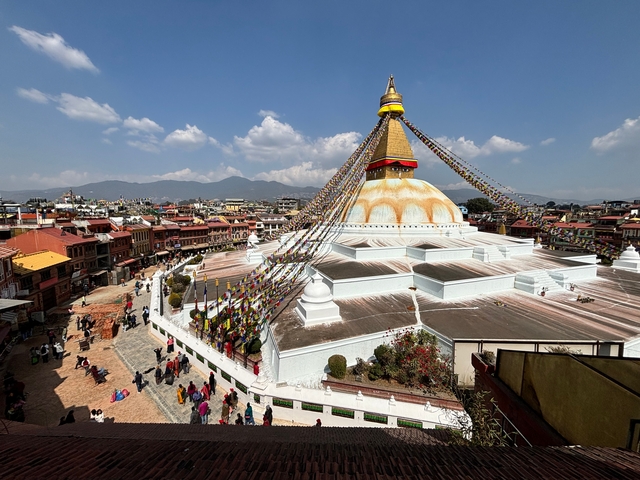       View from above of Boudhanath Stupa surrounded by buildings and people.
  