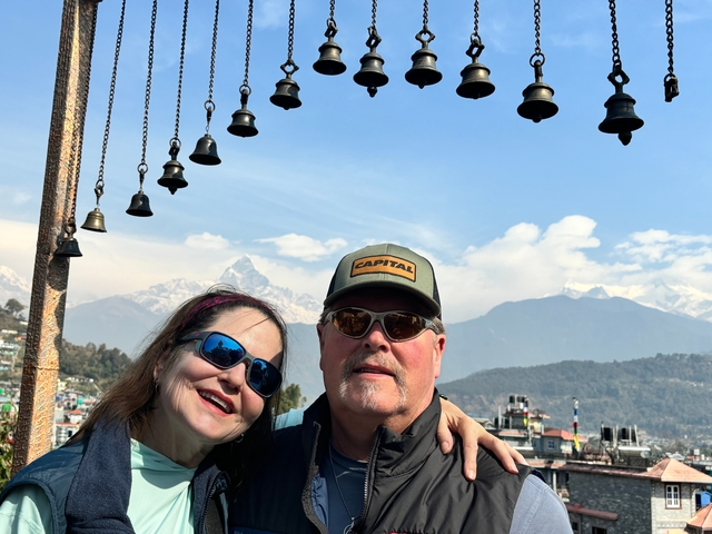      A couple posing with bells and mountains in the background.
  