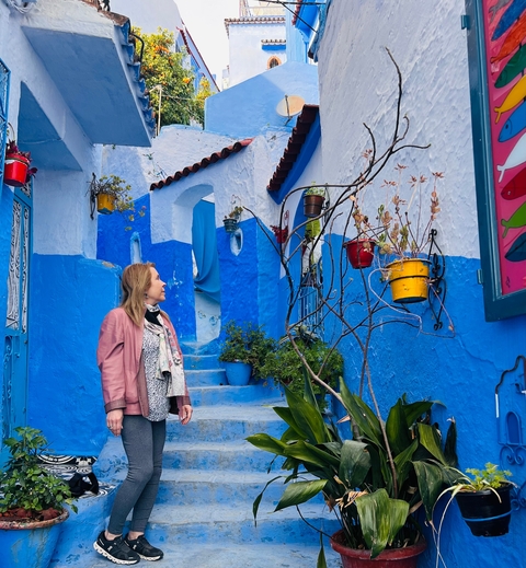 Person in a blue alley with colorful flower pots.