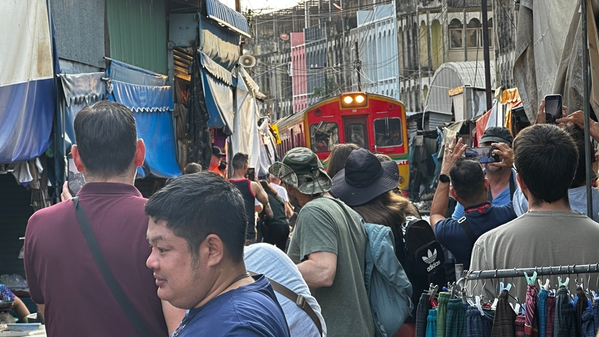       Train passing through a bustling market with many onlookers.
  