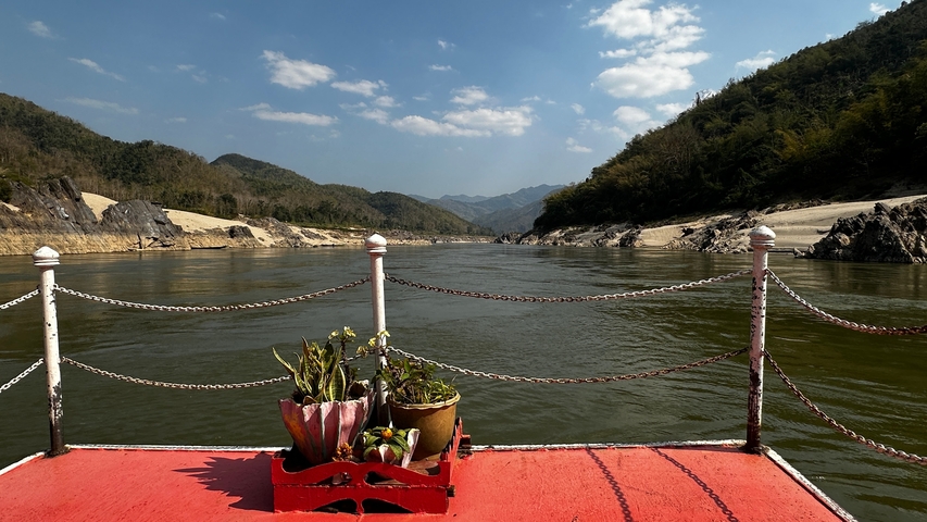       View from a boat on a river with scenic mountains and clear skies.
  