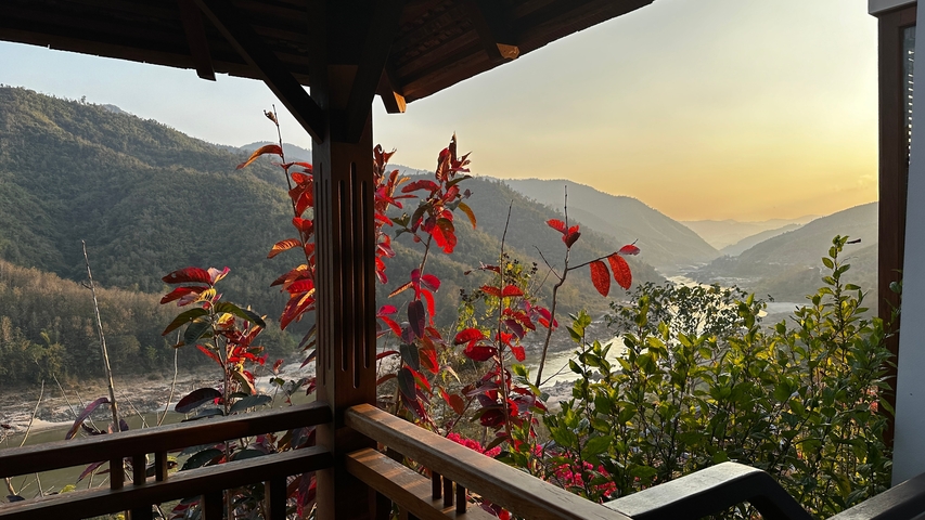       Mountain view from a balcony with red foliage, during sunset.
  