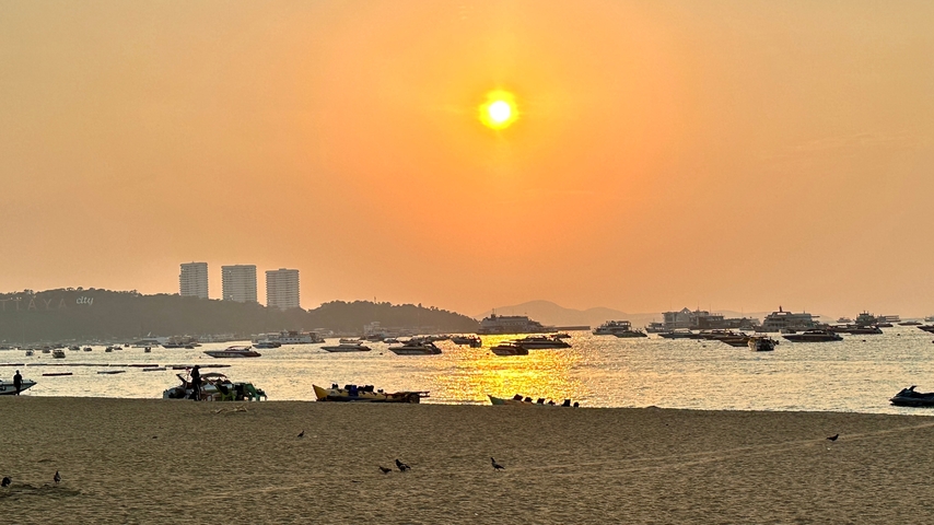       Beach scene at sunset with boats on the water and people on the shore.
  