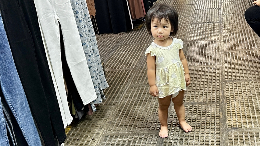 Child standing barefoot in a marketplace corridor.