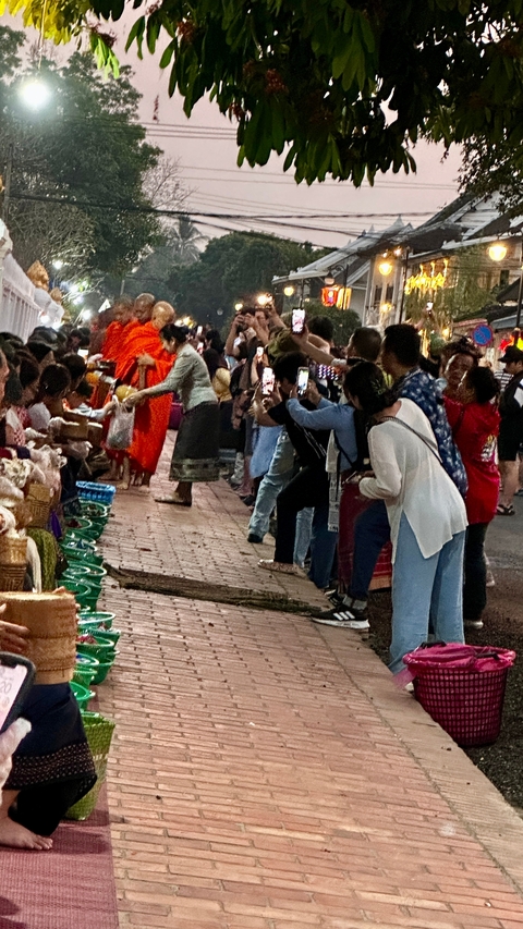 Monks on their morning alms round with locals lining the street.