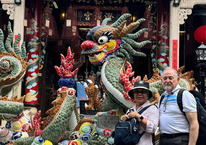 Two tourists posing in front of a colorful dragon statue.