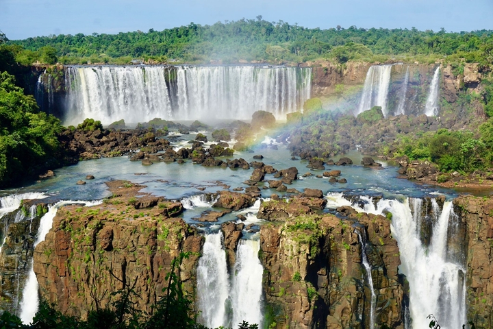       Grand waterfall with rainbow over lush forest.
  