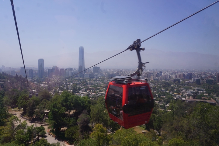 Red cable car over cityscape with distant mountains.