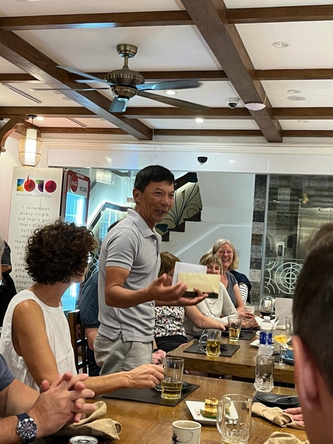 Indoor setting with people listening to a host holding an envelope.