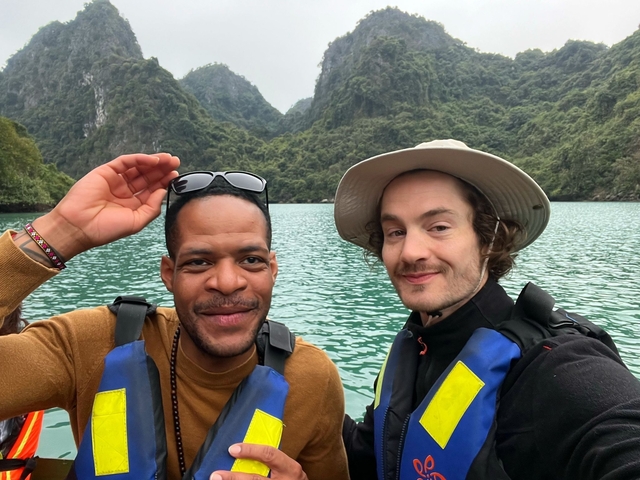       Two people in life jackets with a scenic view of water and limestone karsts behind.
  