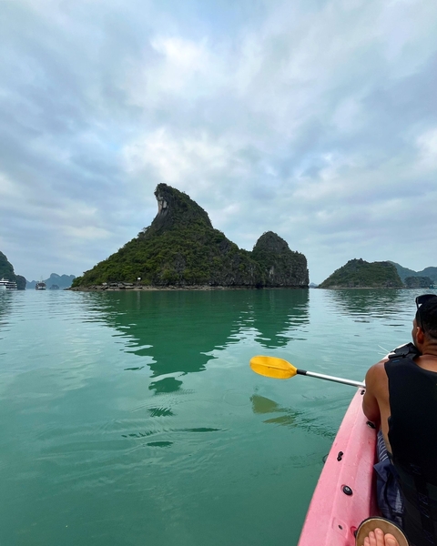       A tranquil view of limestone karsts in calm water with a kayak paddle in view.
  