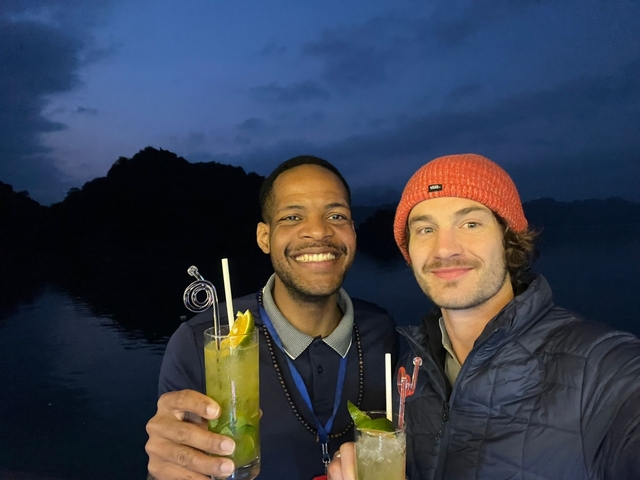       Two people holding drinks at night with mountains silhouetted in the background.
  