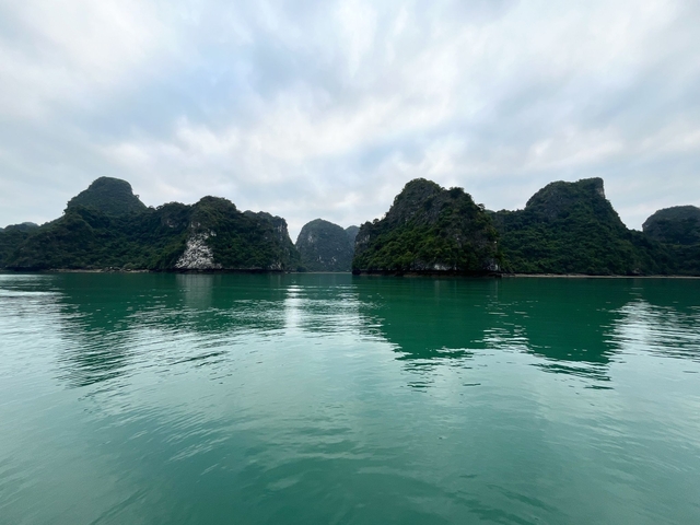       A serene view of limestone cliffs reflected in calm emerald waters.
  