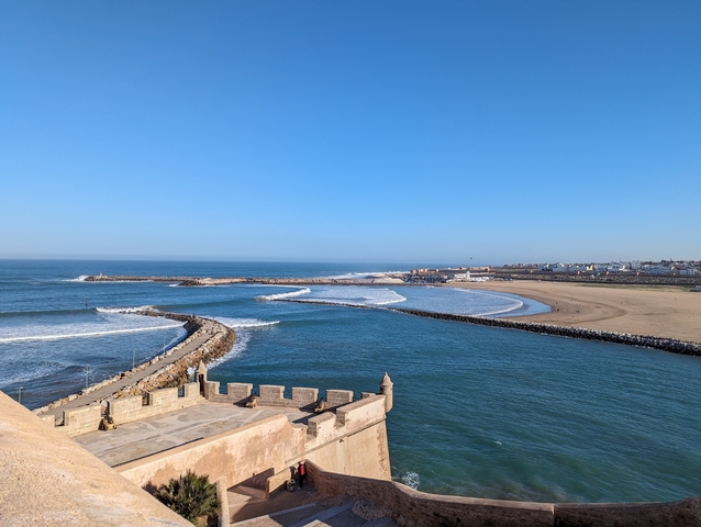       Seaside view with waves and a rocky pier.
  