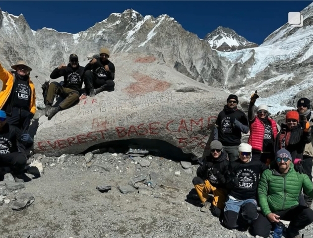       Group of trekkers at Everest Base Camp with a sign.
  