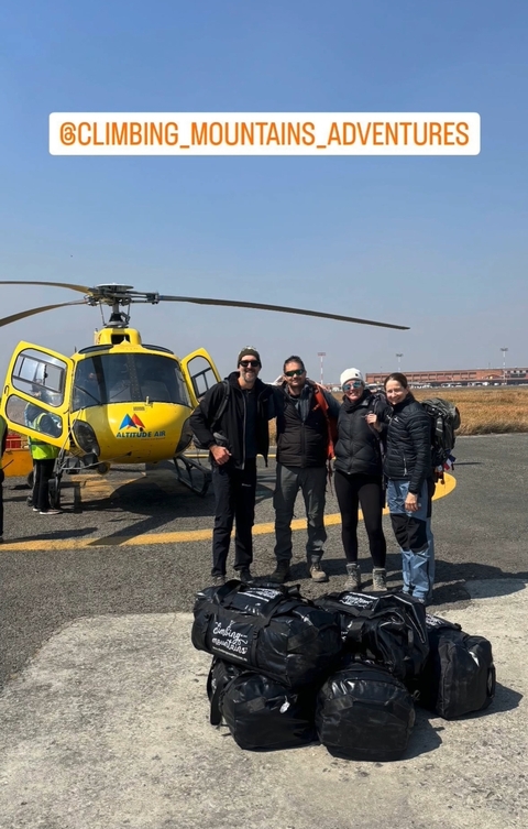       Tourists posing in front of a helicopter on a tarmac.
  