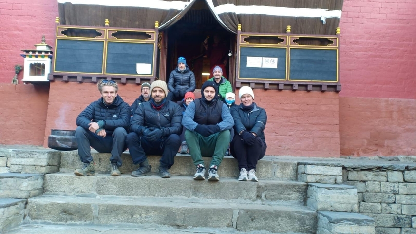       Group sitting on the steps of a red temple building.
  