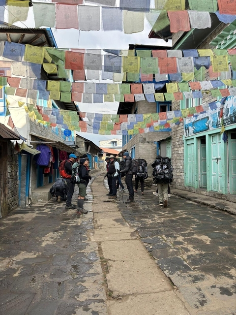       Group of trekkers walking through a village with flags.
  