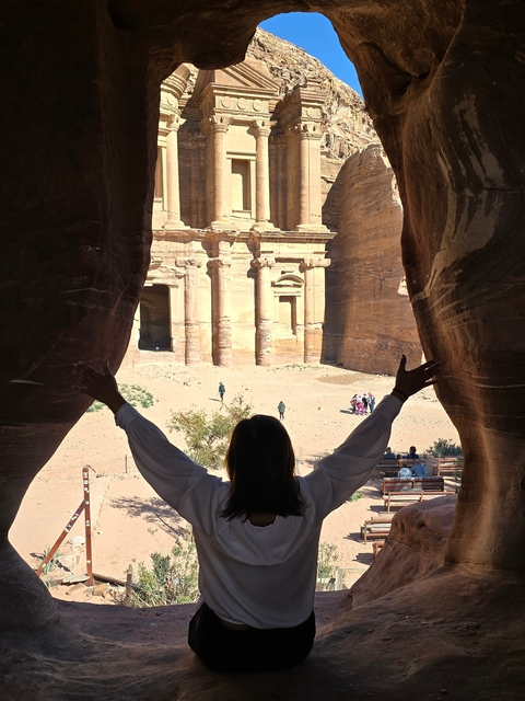 A person standing at a rock entrance facing Petra