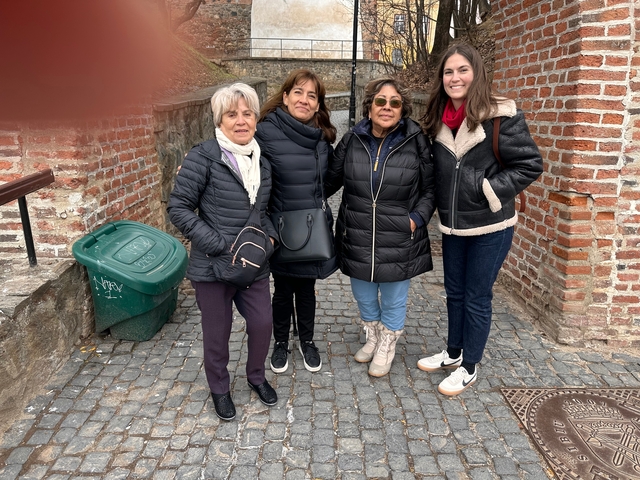       Four people standing on a cobblestone street near a brick wall.
  