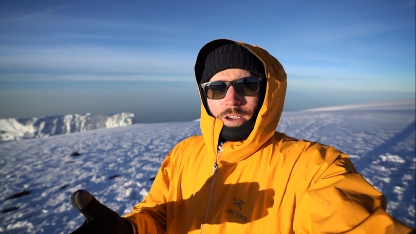 Man in a bright yellow jacket standing on a snowy mountain.