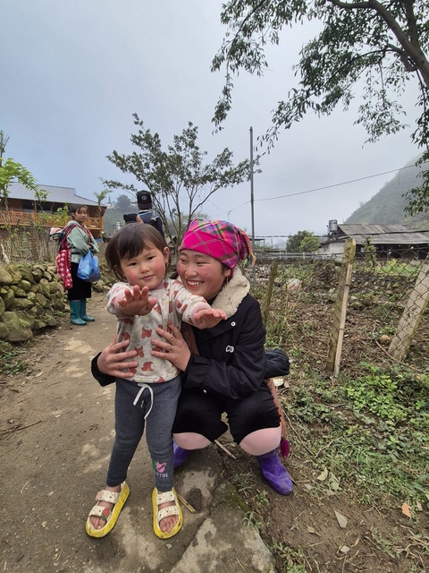       Woman holding a child on a path with buildings in the background.
  