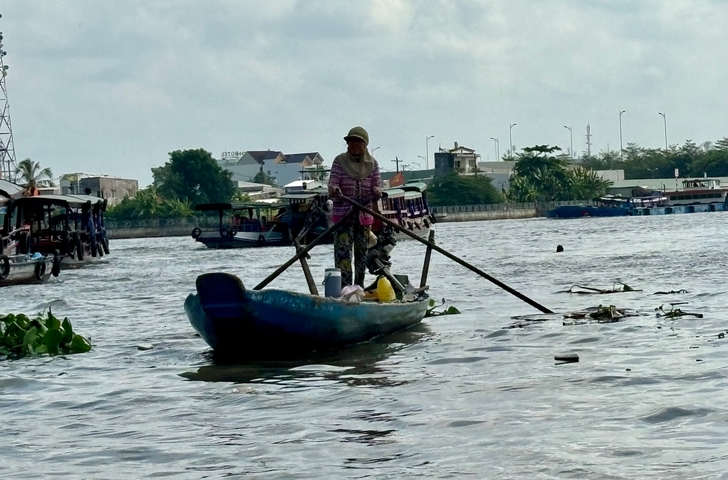       Person paddling a wooden boat on a river, surrounded by other boats and buildings.
  