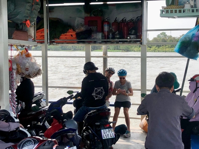       People on a ferry crossing a river with motorbikes and supplies.
  