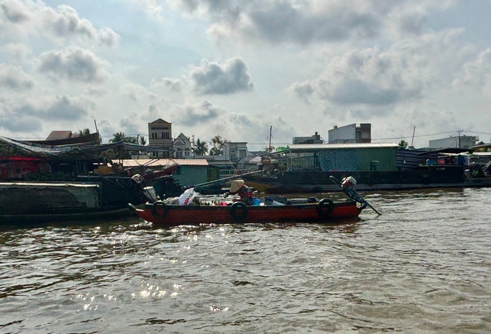       A small wooden boat in a river lined with buildings and other boats.
  