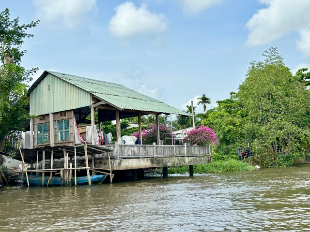 Riverside house on stilts with flowering plants.