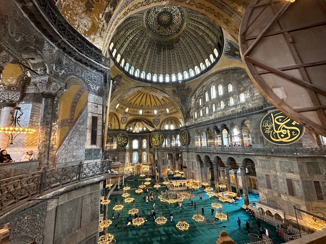       Interior of Hagia Sophia with ornate decorations and visitors.
  