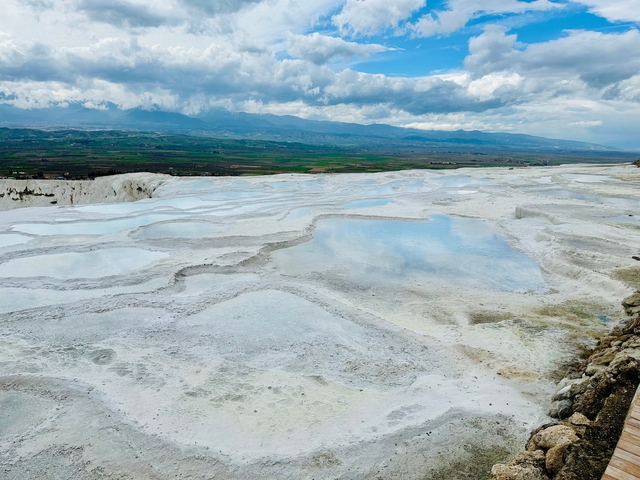 Mineral-rich terraces with turquoise pools against a mountainous backdrop.