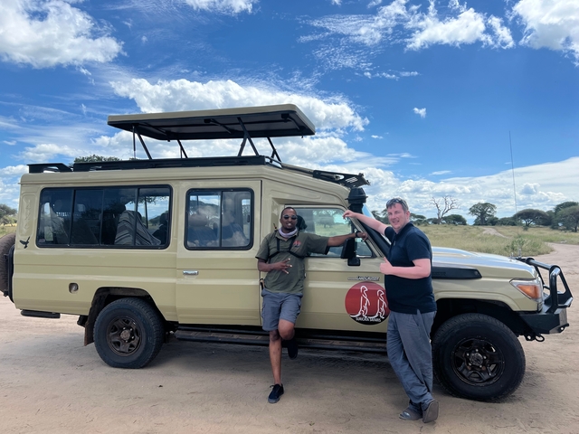 Two men posing with a safari vehicle under a blue sky.