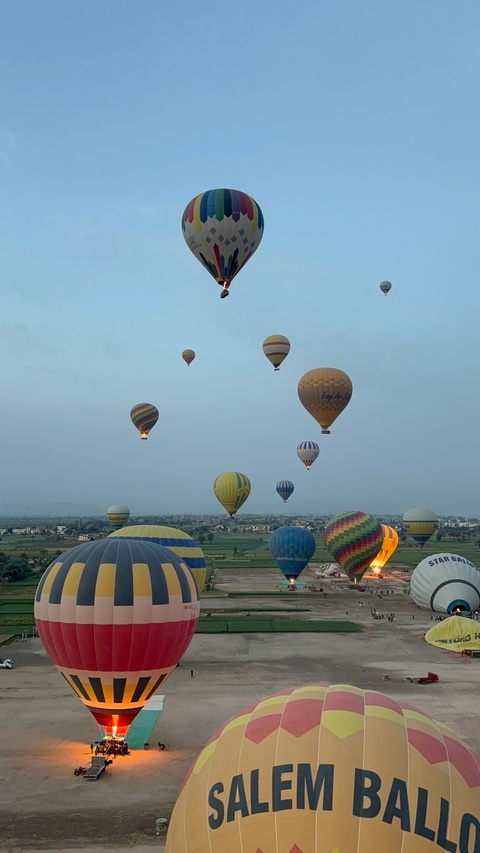 Multiple hot air balloons floating over a village landscape.