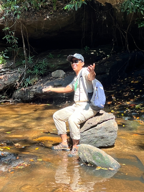Man sitting on a rock in a stream looking joyful.