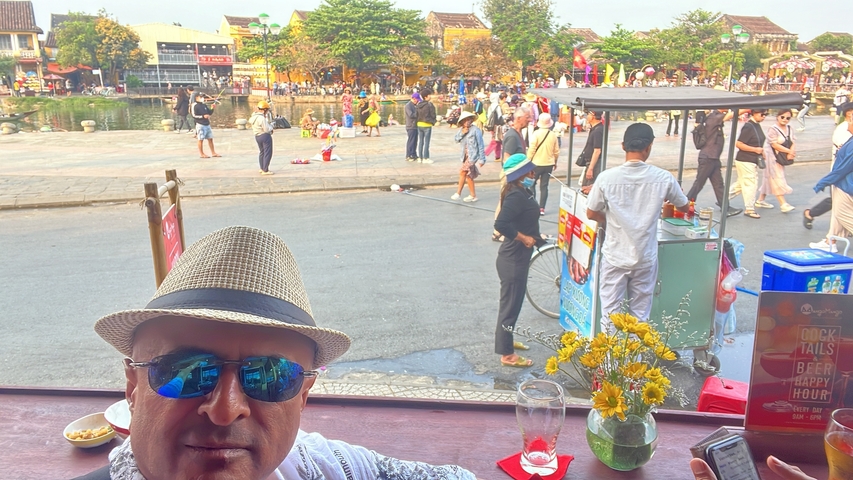 Man wearing a hat sitting at a cafe with a street view.