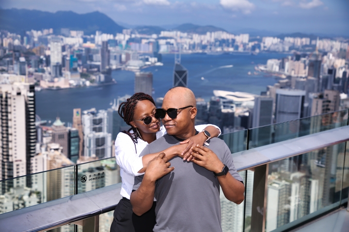 Couple posing on a glass balcony with a city skyline in the background.