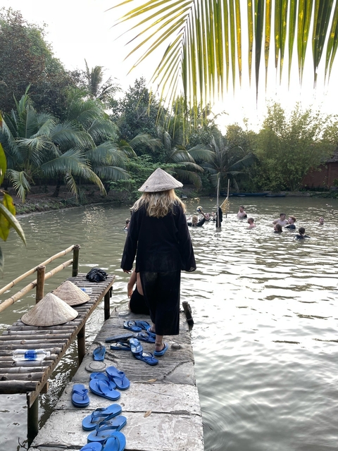       People in a waterway surrounded by trees wearing traditional hats.
  