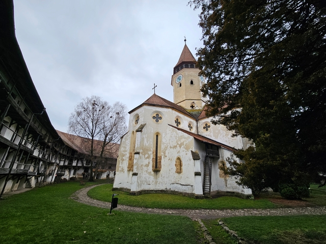 Old fortified church with Gothic architecture in a courtyard surrounded by trees and a pathway.