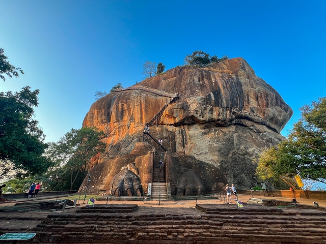 Sigiriya Rock Fortress with stairs leading up and tourists climbing.